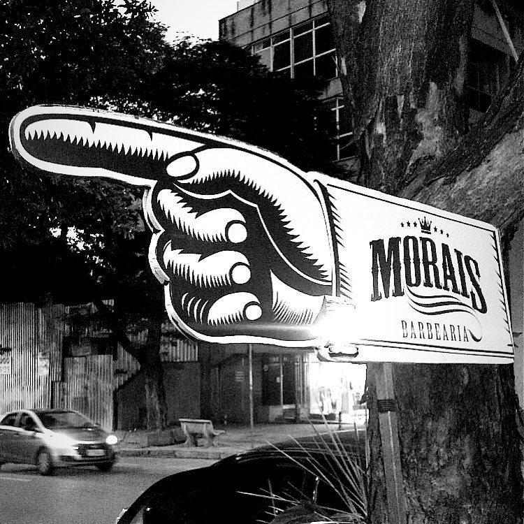 Placa da Morais Barbearia em forma de mão apontando, presa numa árvore da calçada
