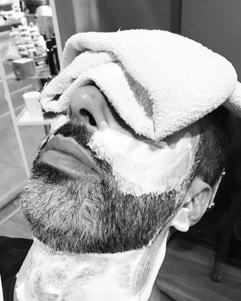 Cliente deitado com toalha quente sobre os olhos e espuma de barbear no rosto